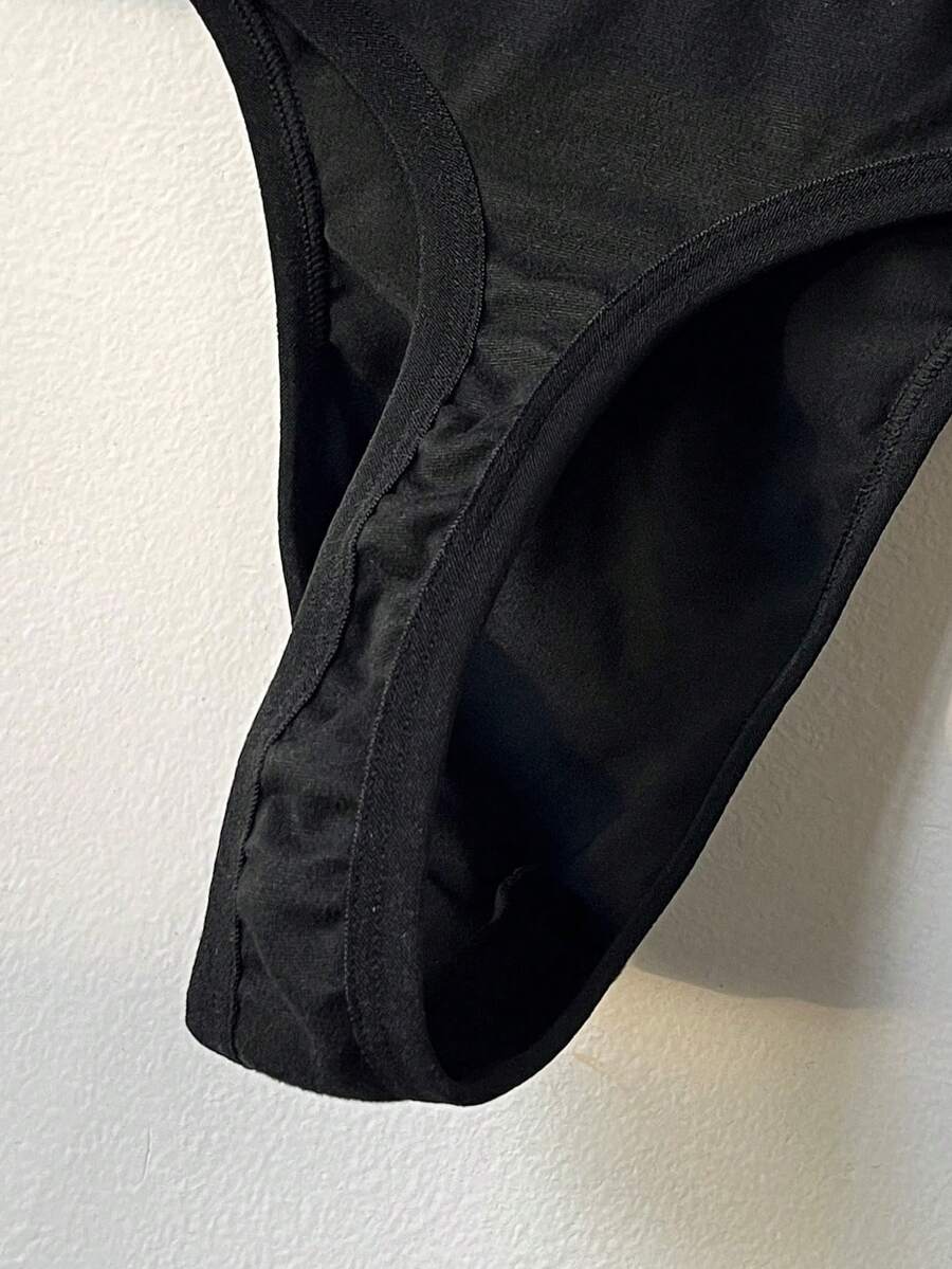 Black low-rise men's thong underwear with letter print pattern made of knitted fabric.