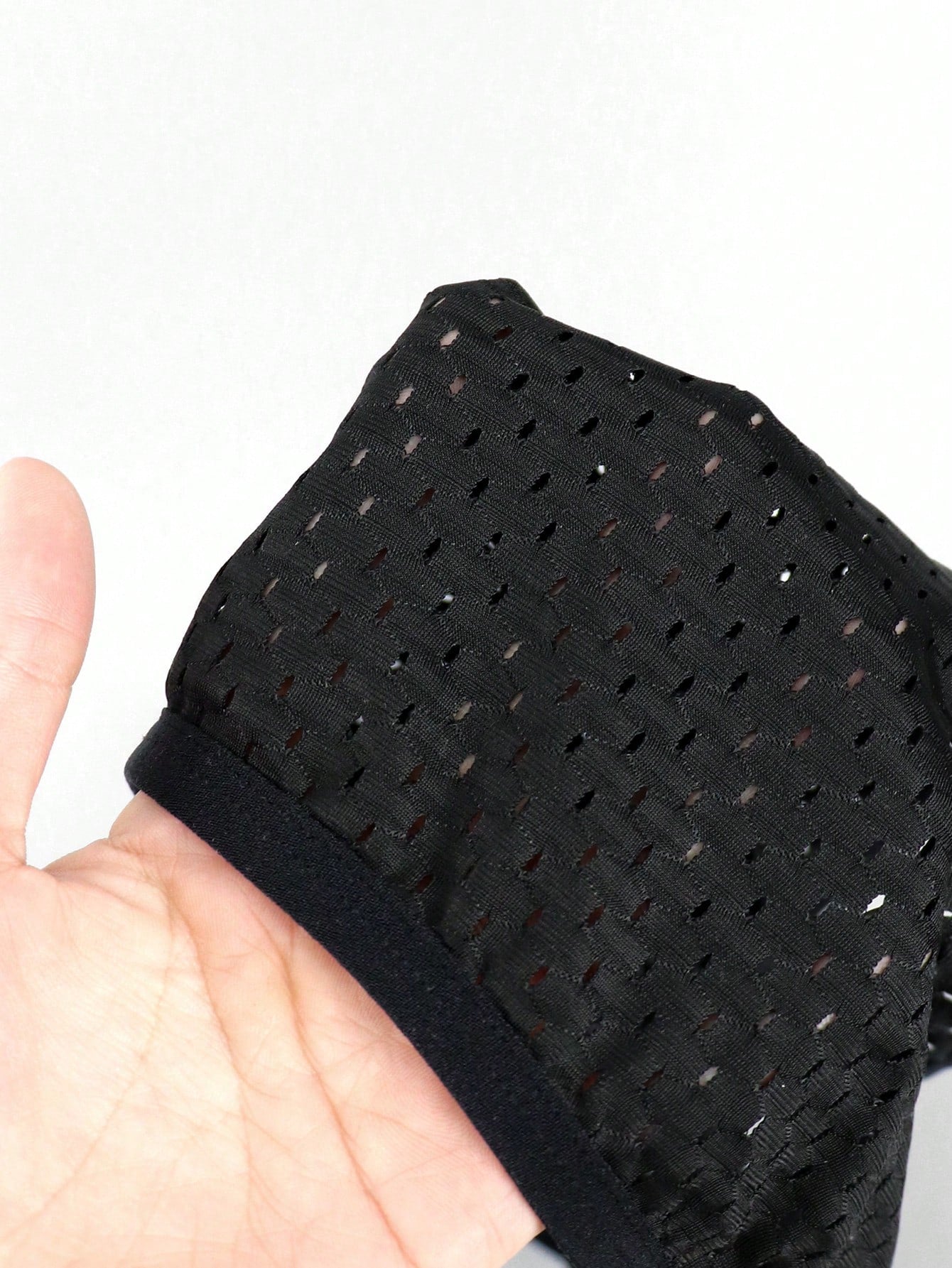 Men's black low rise thong underwear in knitted mesh with tie dye pattern, cut out detail, and medium stretch fabric.