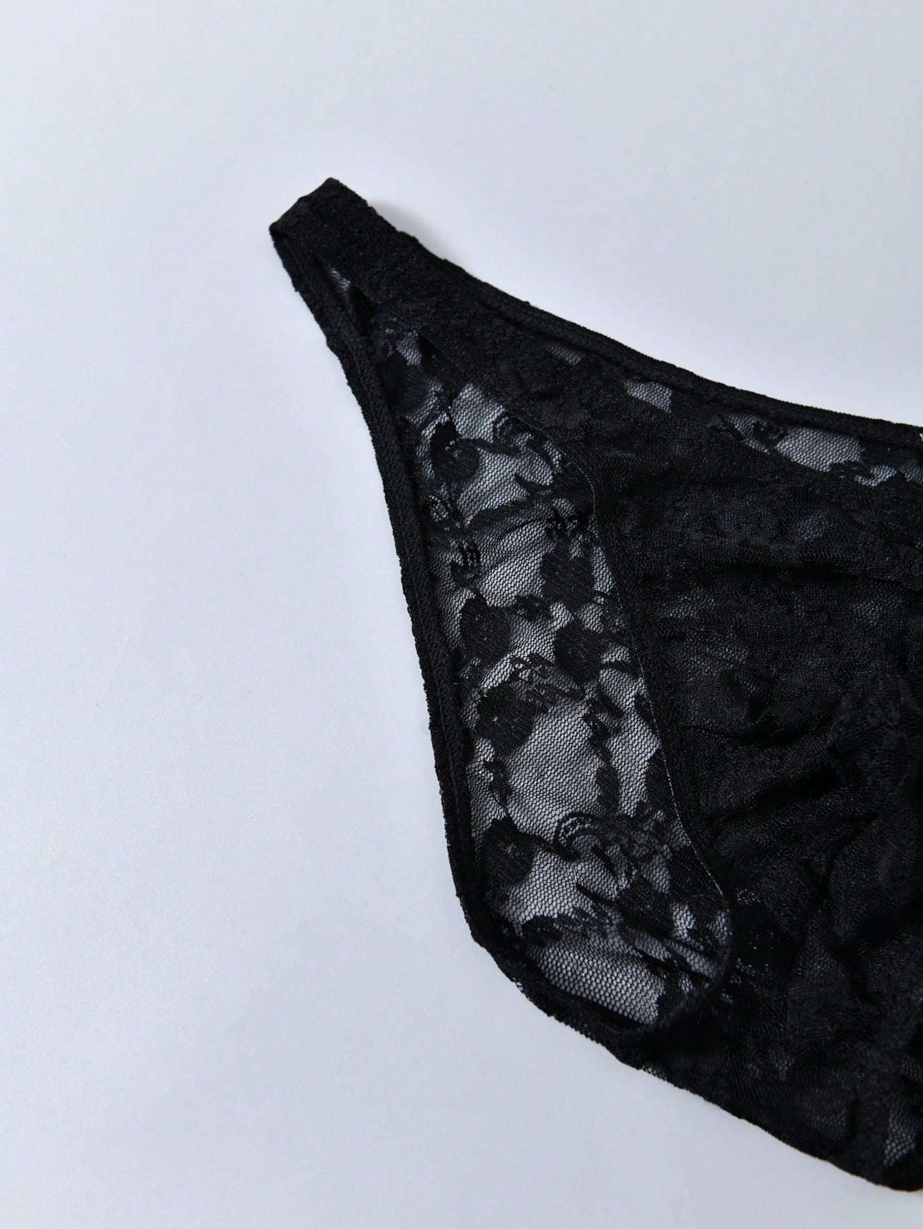 Men's black lace thong underwear with low rise fit, contrast lace detail, and T-back design in medium-stretch polyester elastane fabric.