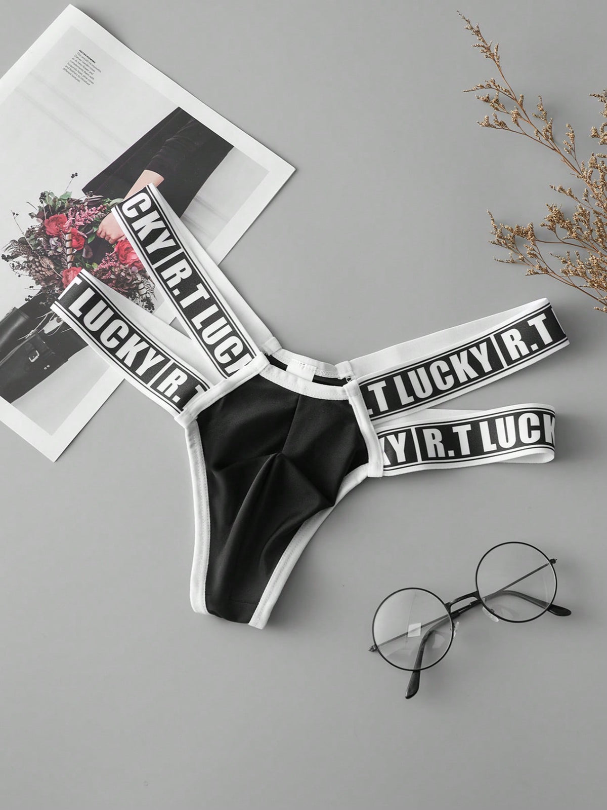 Black low-rise men's thong underwear featuring a belted waist detail and letter pattern on knitted fabric.