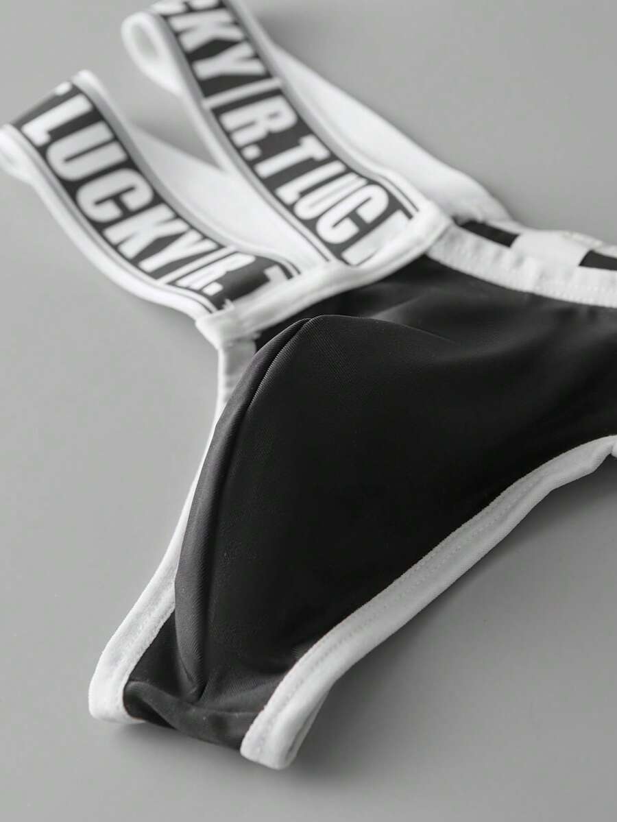 Black low-rise men's thong underwear featuring a belted waist detail and letter pattern on knitted fabric.