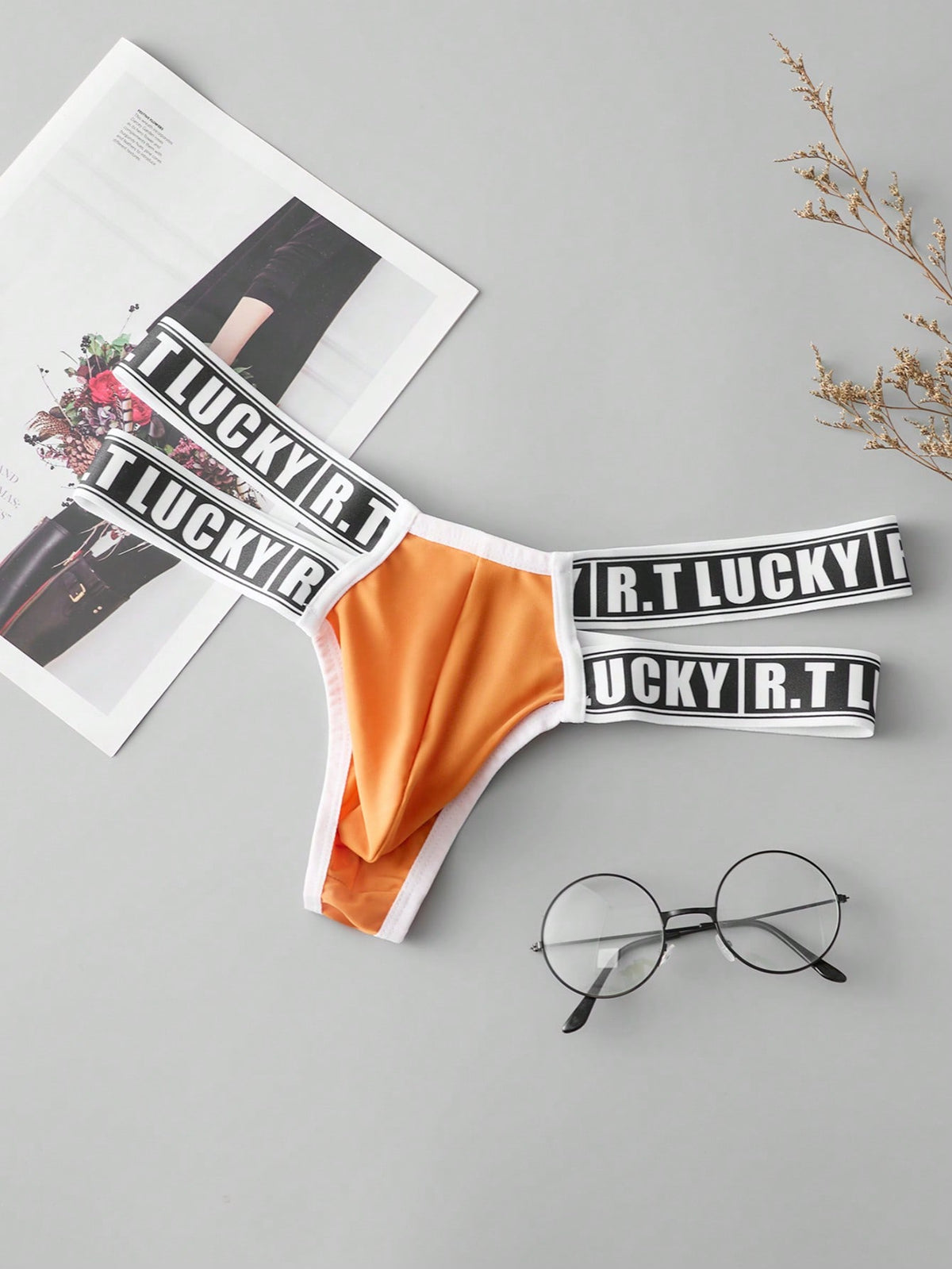 Black low-rise men's thong underwear featuring a belted waist detail and letter pattern on knitted fabric.