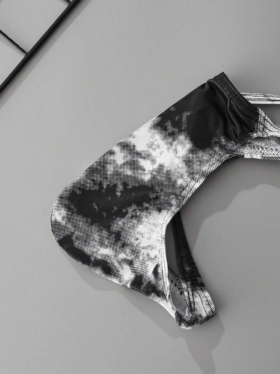Black men's low rise thong underwear featuring asymmetrical tie dye design made from knitted polyester fabric.