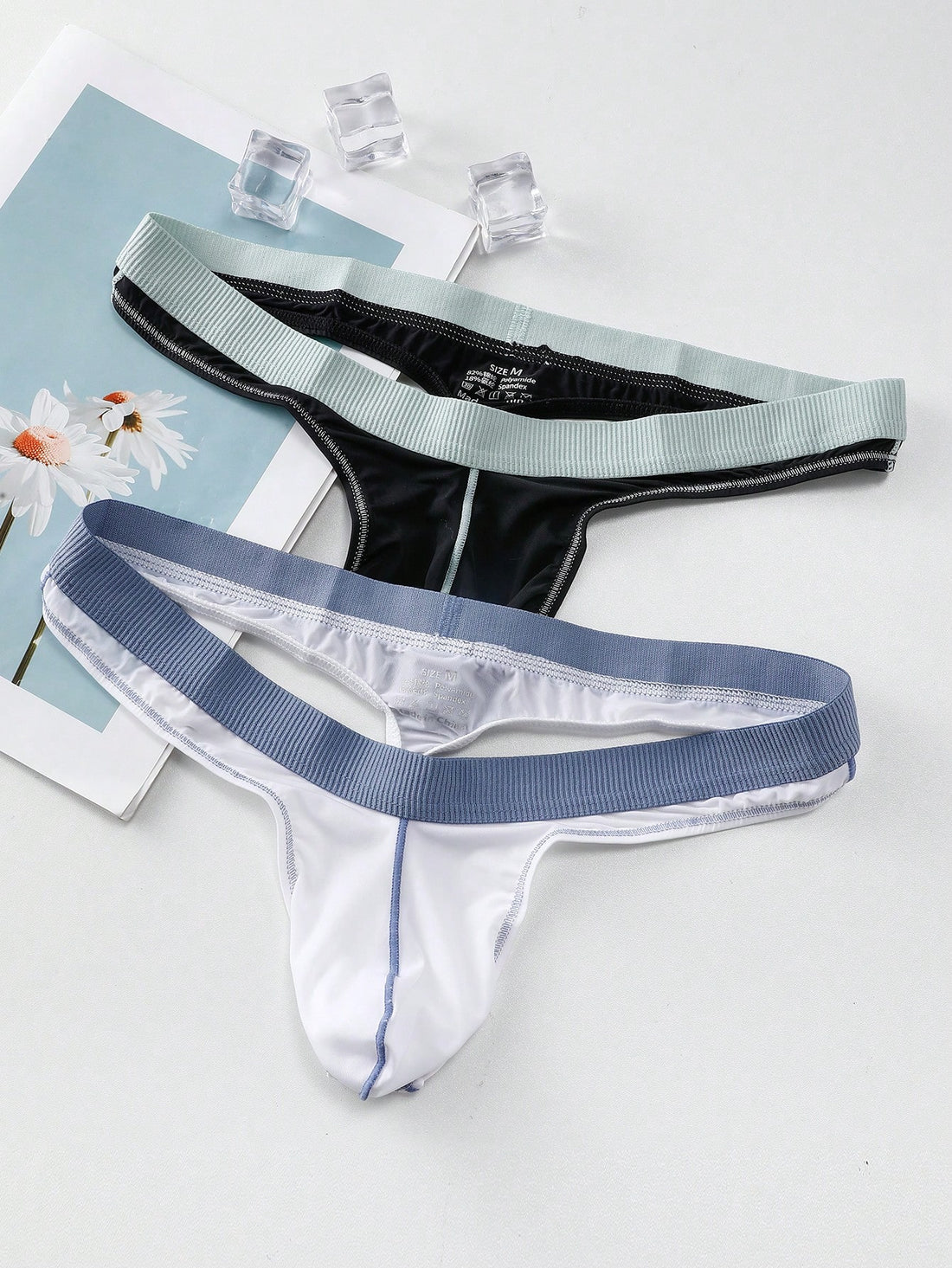 Set of two men's low-rise thong underwear featuring multicolor plant print and contrast waistband.