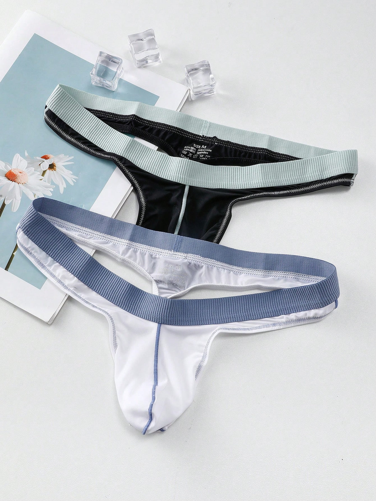 Set of two men's low-rise thong underwear featuring multicolor plant print and contrast waistband.