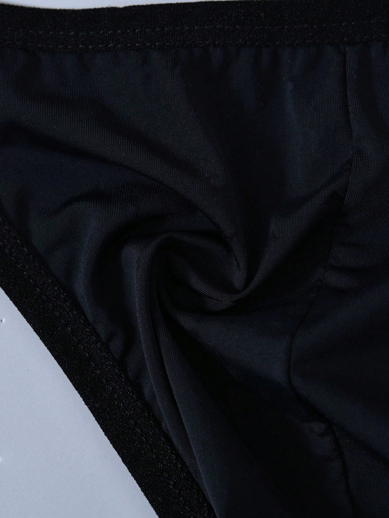 Men's mid rise thong underwear with textured pattern and letter-style tape waistband, made from polyester elastane stretch fabric.