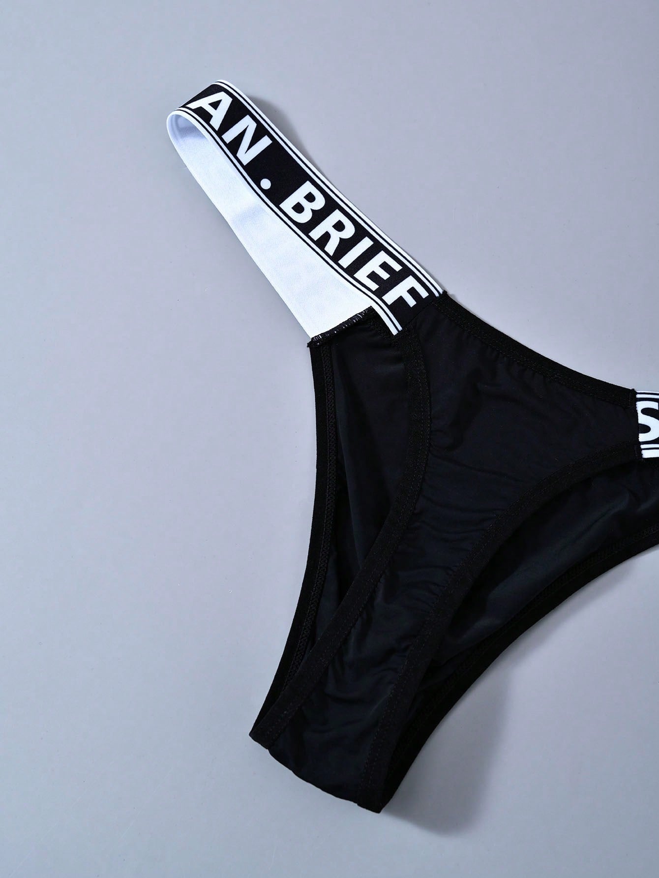 Men's mid rise thong underwear with textured pattern and letter-style tape waistband, made from polyester elastane stretch fabric.