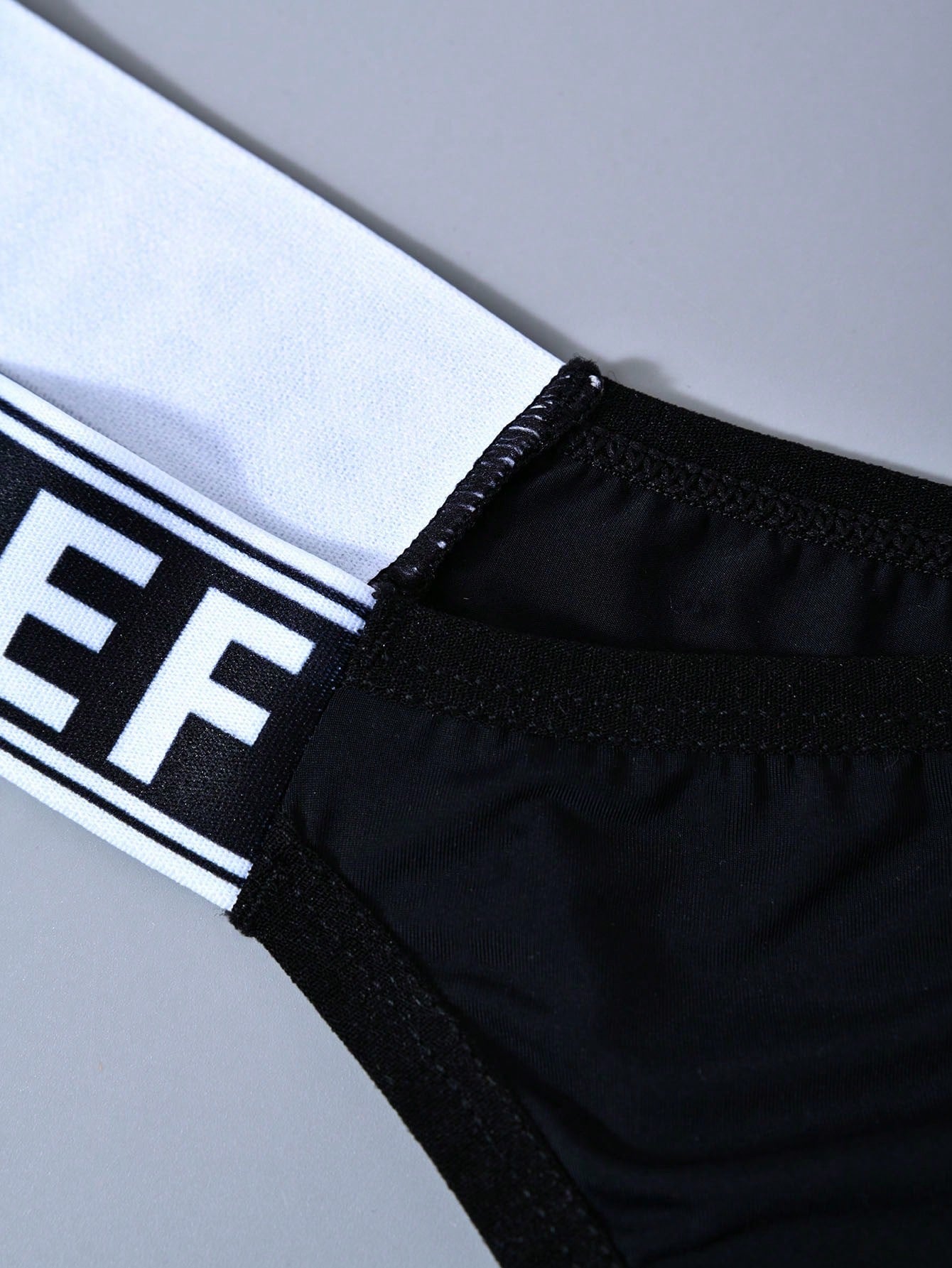 Men's mid rise thong underwear with textured pattern and letter-style tape waistband, made from polyester elastane stretch fabric.