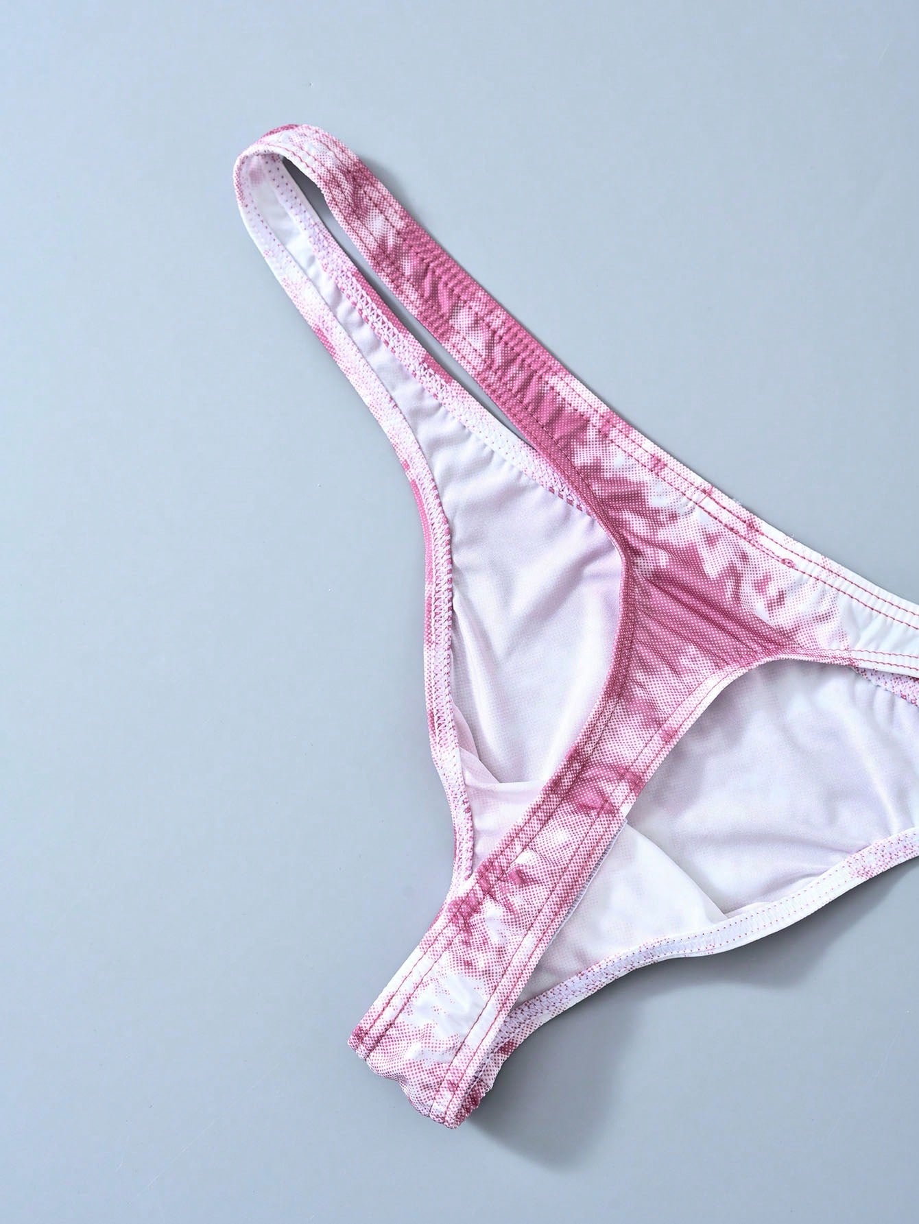 Men's tie dye thong underwear with a low rise fit and T-back design, made from polyester and elastane stretch fabric.