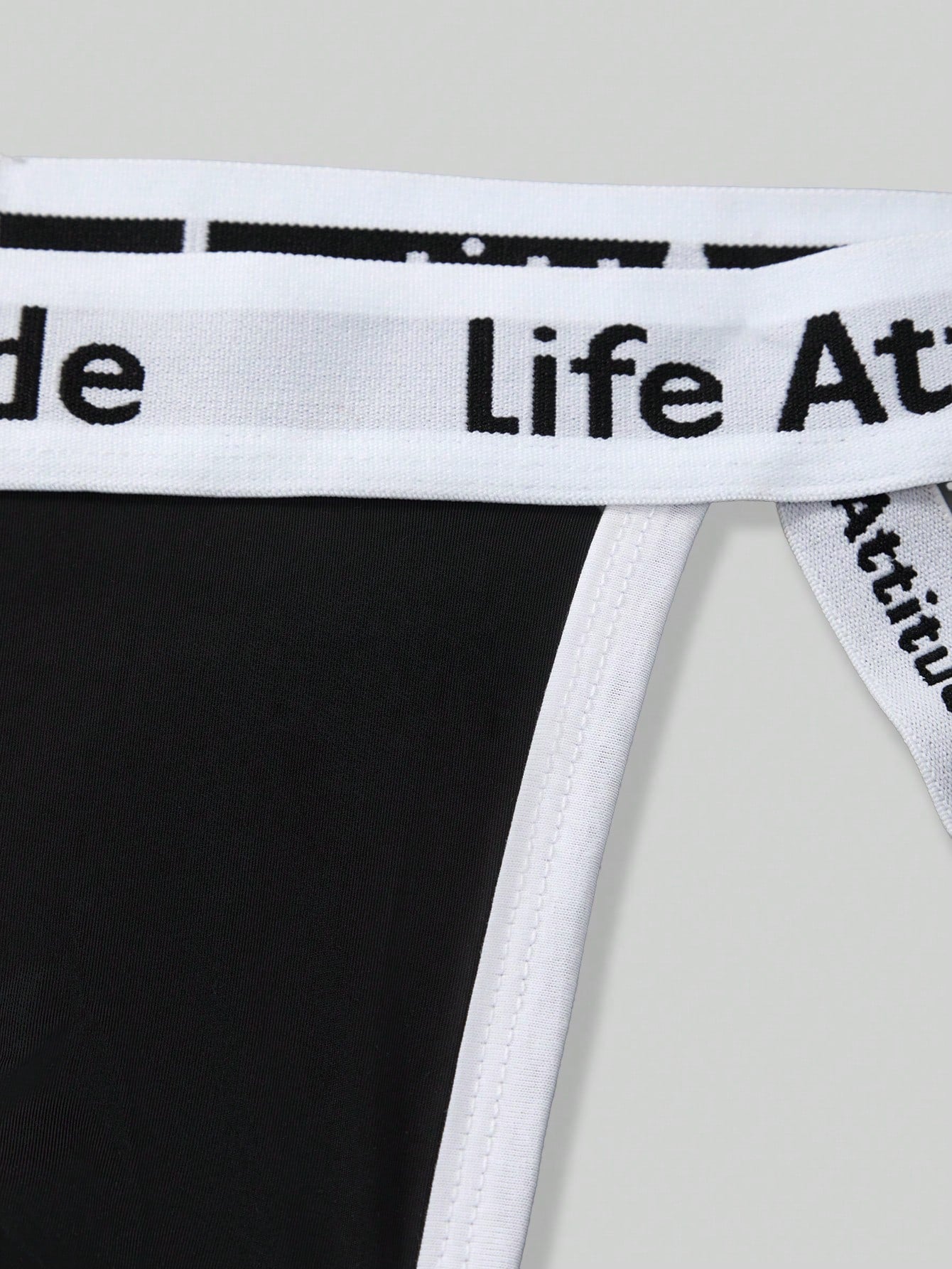 Men's black low rise thong underwear in knitted fabric with letter and striped pattern, medium stretch, made from polyamide and elastane.