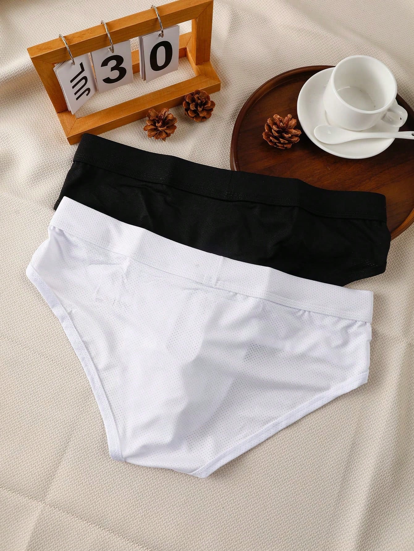 Men's low rise mesh briefs with letter graphic pattern, multicolor design, patched detail, zipper accent, and medium stretch polyester elastane fabric.