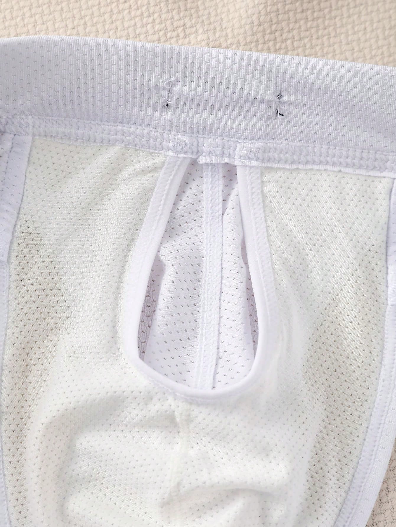 Men's low rise mesh briefs with letter graphic pattern, multicolor design, patched detail, zipper accent, and medium stretch polyester elastane fabric.