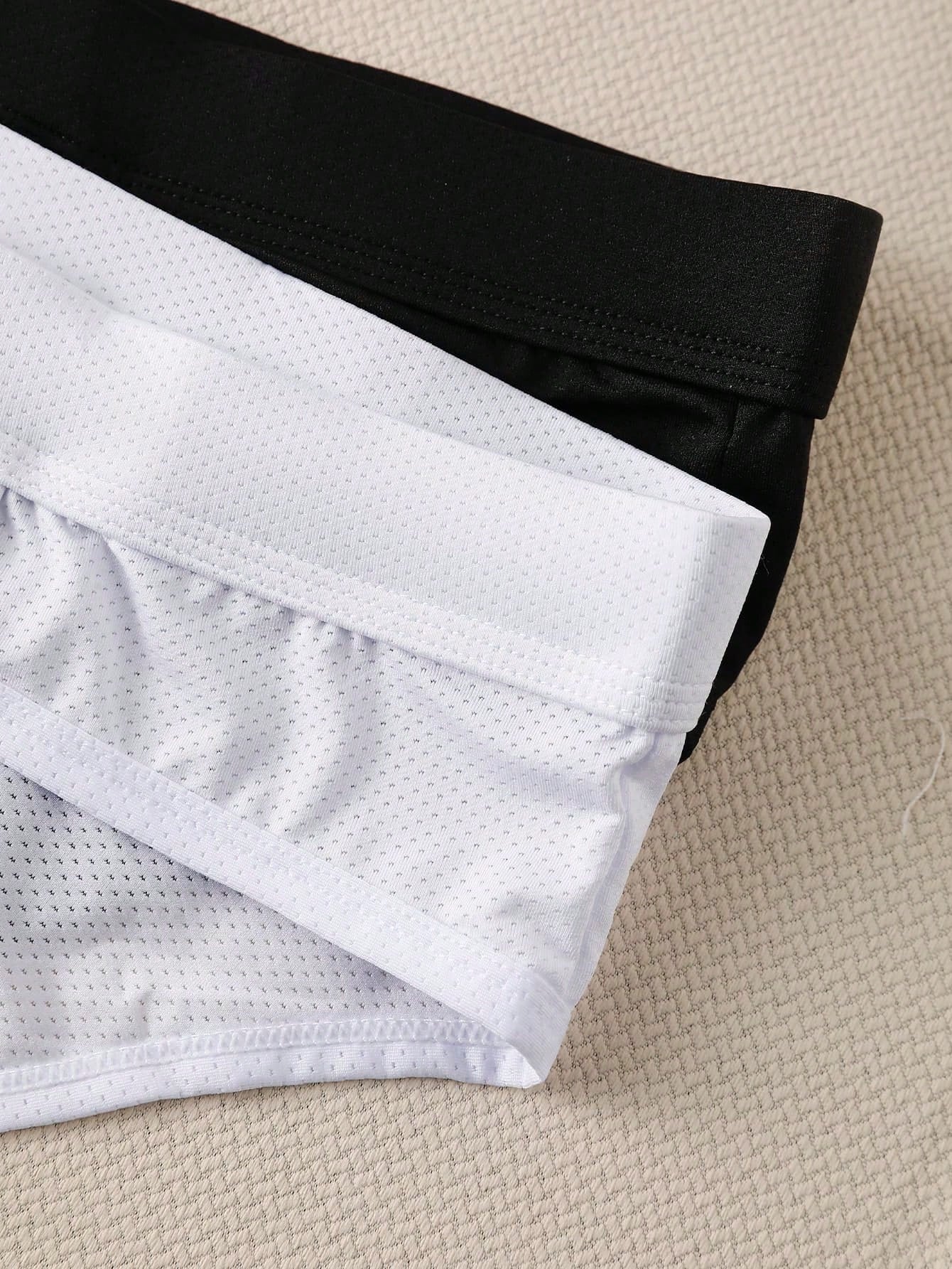Men's low rise mesh briefs with letter graphic pattern, multicolor design, patched detail, zipper accent, and medium stretch polyester elastane fabric.