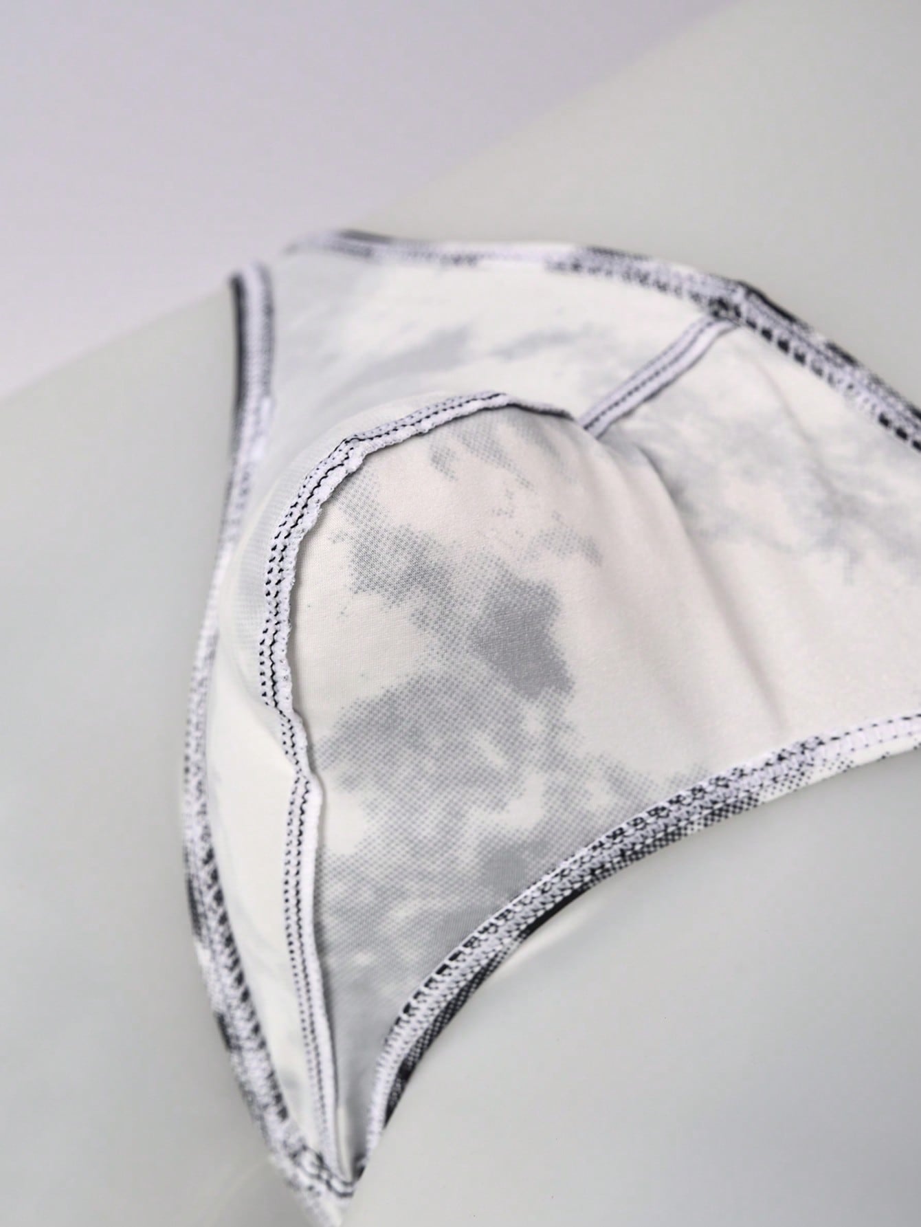 Men's tie dye thong underwear with a low rise fit and T-back design, made from polyester and elastane stretch fabric.