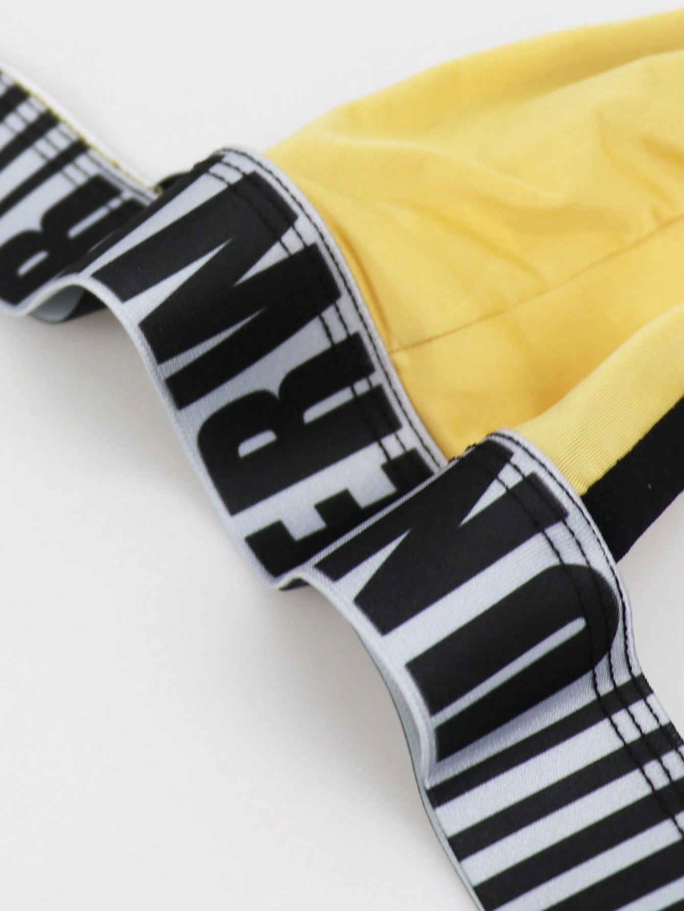 Men's low rise thong underwear in knitted fabric with striped colorblock pattern and letter waistband.