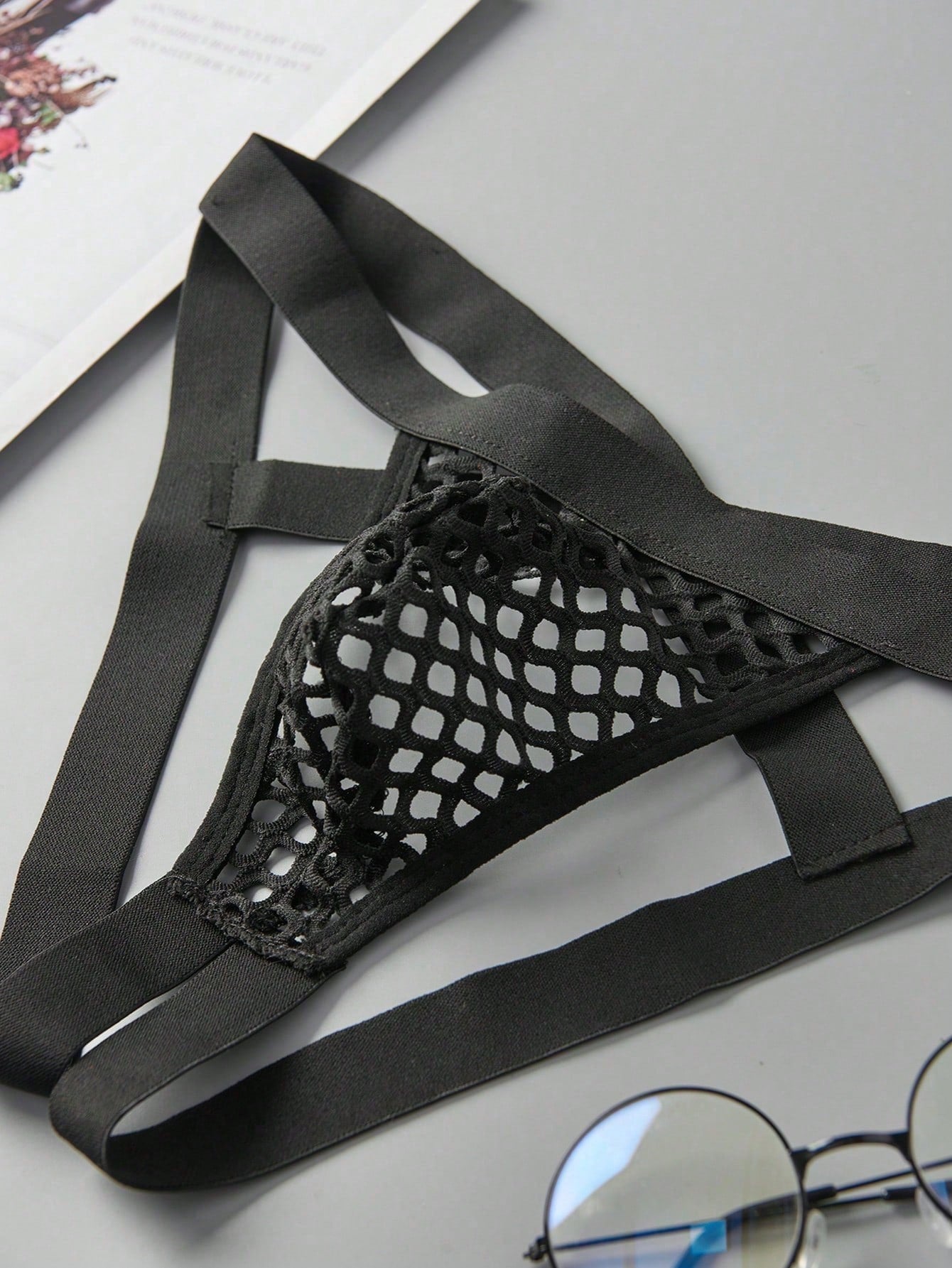 Black men's low rise thong underwear in semi-sheer mesh tulle with geometric pattern and criss cross cut-out detail.