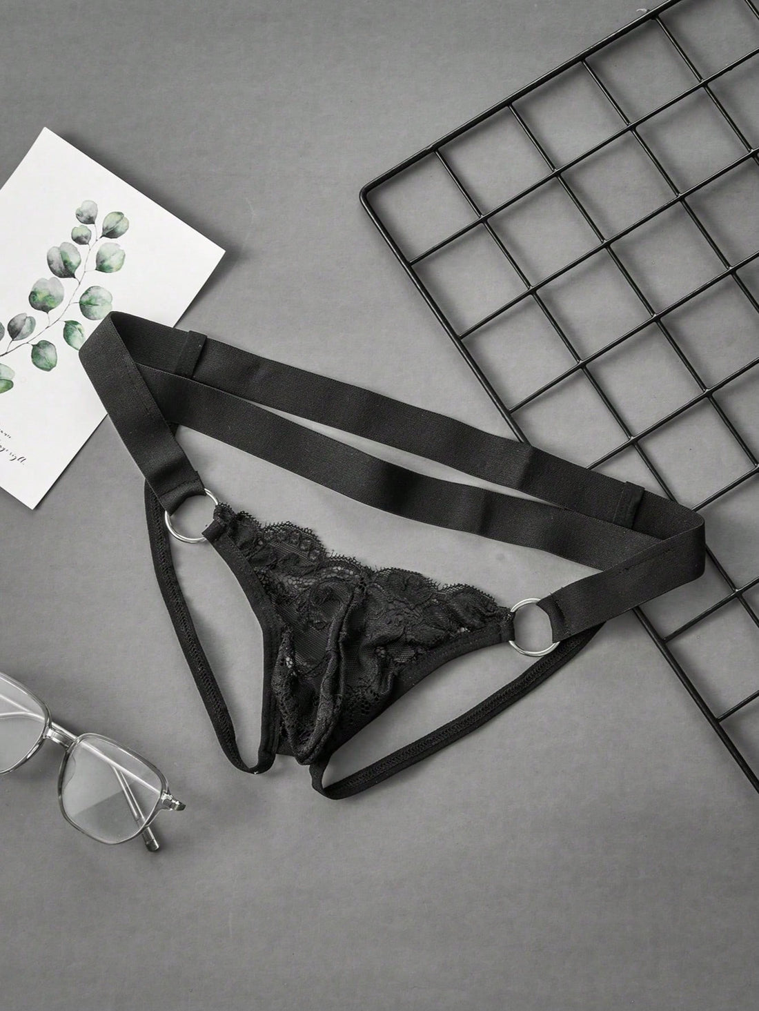 Black men's low-rise lace jockstrap underwear featuring hollow-out details and semi-sheer fabric.
